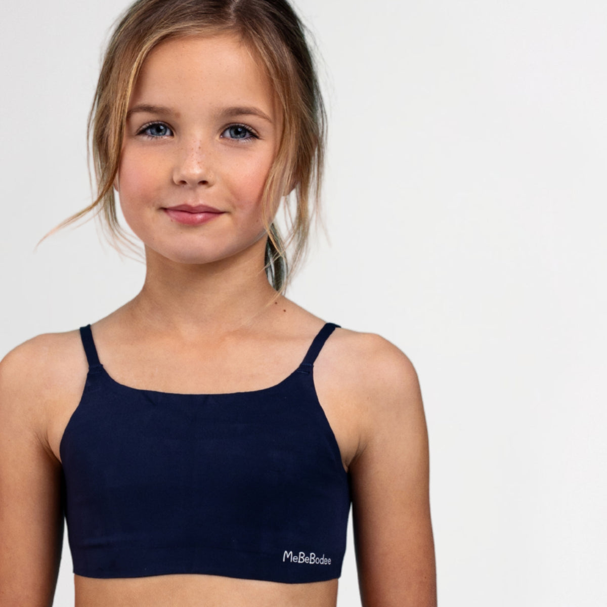 Young girl wearing a navy blue sports bralette with 'MeBeBodee' branding on a white background