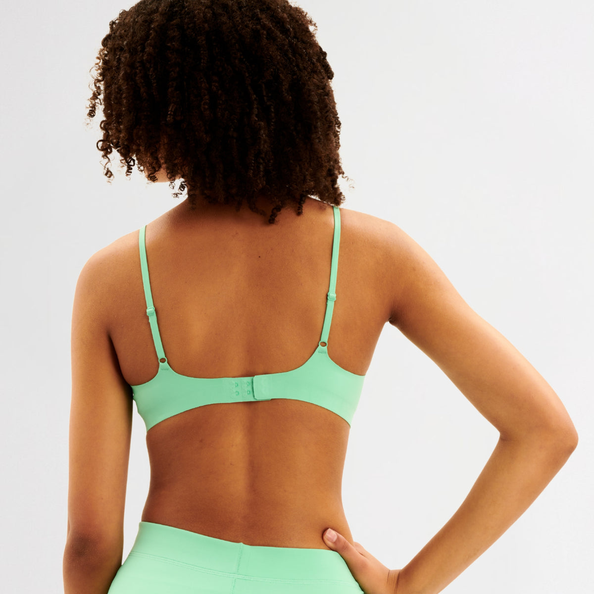 Back of teen girl wearing a green bra and leggings on a light gray background