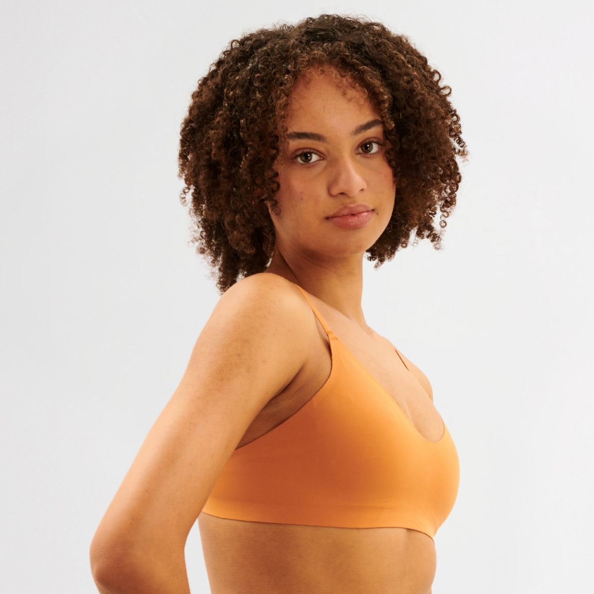 Teen Girl wearing an caramel coloured bra against a plain background