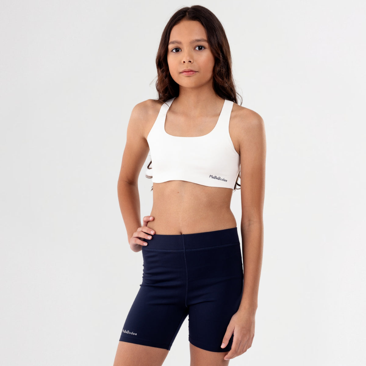 Teen Girl wearing a white sports bra and navy shorts on a plain background