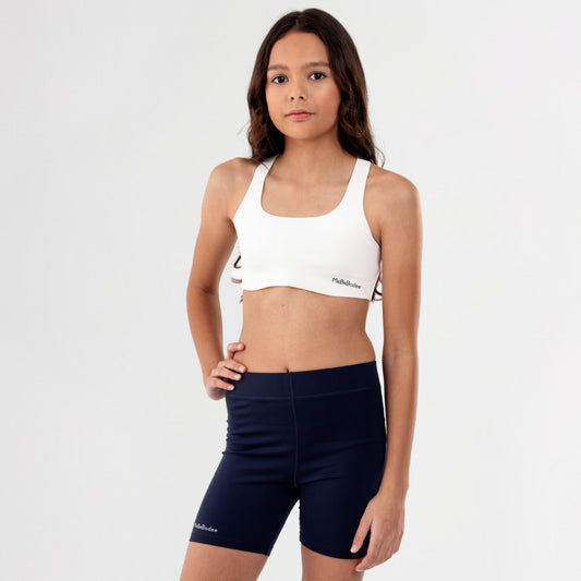 Teen Girl wearing a white sports bra and navy shorts on a plain background