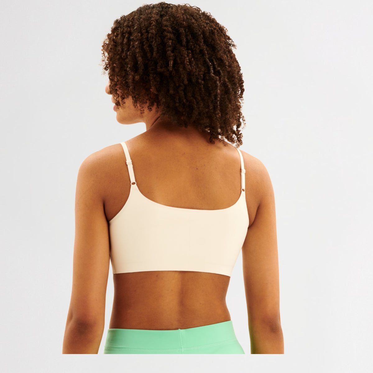 Back of teen girl wearing a white sports bralette and green shorts on a light gray background
