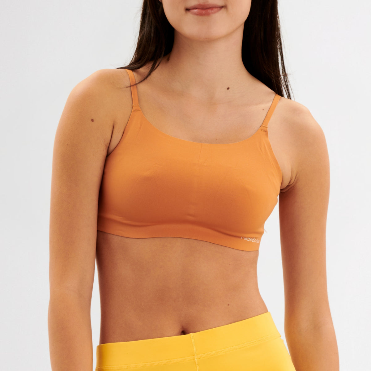 Teen girl wearing a caramel sports bralette and yellow pants on a white background