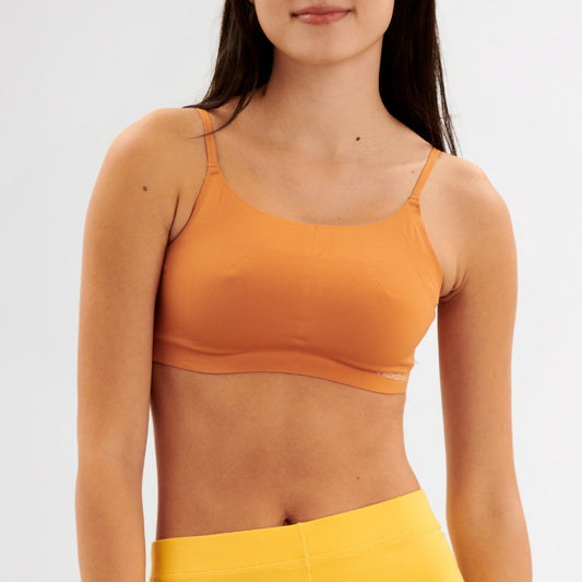 Teen girl wearing a caramel sports bralette and yellow pants on a white background