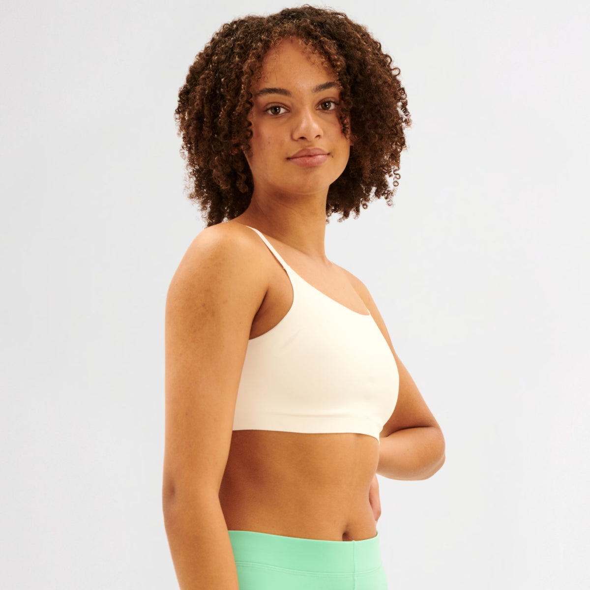 Teen girl wearing a white sports bralette and green leggings on a plain background