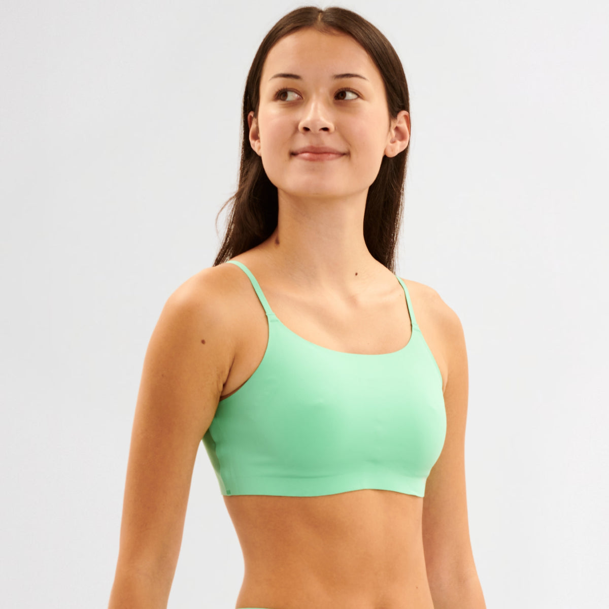 Teen Girl wearing a green sports bralette against a light gray background