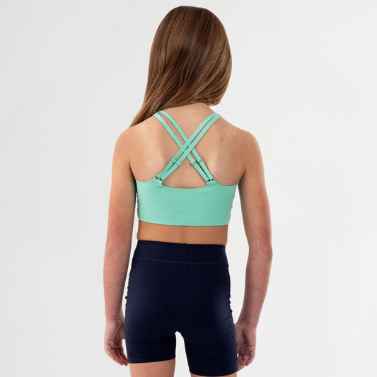Back of Girl wearing a green crossed back sports bra and black shorts on a white background