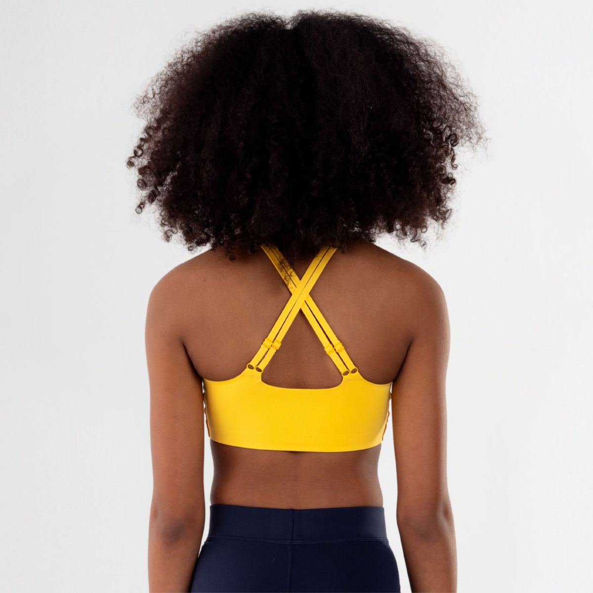 Back of Tween Girl wearing a yellow crossed strap sports bra and black leggings on a white background