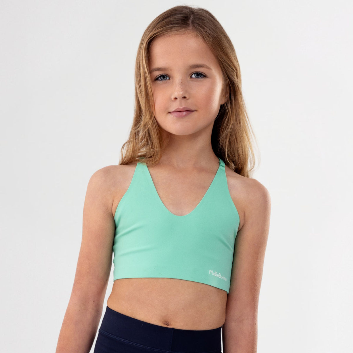 Tweeen girl wearing a green sports bra and black leggings on a white background
